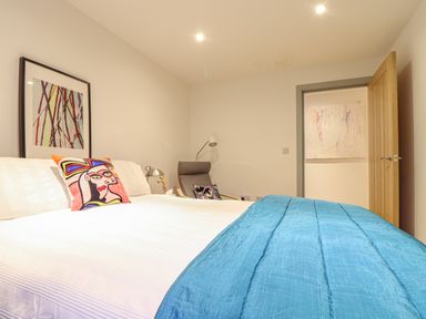 A bedroom with a double bed a blue blanket a chair with a cushion and an open door showing a painting at Idlewild 2 Wheal Turnavore in St Agnes
