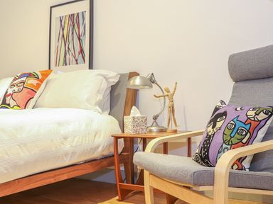 A bedroom with a wooden bed with white bedding a side table with a lamp and mannequin and a grey armchair with a colorful pillow at Idlewild 2 Wheal Turnavore in St Agnes