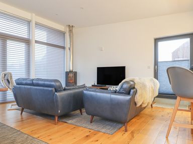 A living room with leather sofas a wood floor a television and a window with blinds at Idlewild 2 Wheal Turnavore in St Agnes