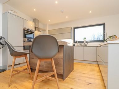 A kitchen with grey cabinets a wooden island and two grey chairs at Idlewild 2 Wheal Turnavore in St Agnes