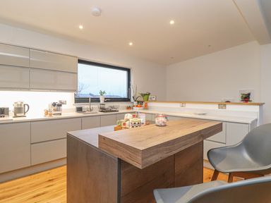 A kitchen with a wooden island countertop two chairs white cabinets and a window at Idlewild 2 Wheal Turnavore in St Agnes