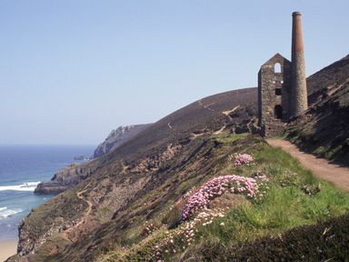 A coastal cliff path with an old stone building and chimney near the ocean at Idlewild 2 Wheal Turnavore in St Agnes