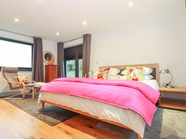 A bedroom with a bed covered by a pink blanket two colorful pillows a chair a wooden floor and a chest of drawers at Idlewild 2 Wheal Turnavore in St Agnes