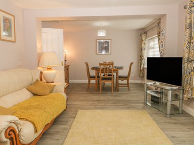 A living room with a sofa, lamp, dining table with chairs, television on a glass stand, and floral curtains at 2 The Close in Robin Hood'S Bay