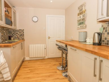 A kitchen with wooden countertops two bar stools a kettle and wall clock at 2 The Close in Robin Hood'S Bay