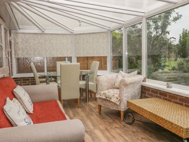 A conservatory with a sofa a floral armchair a glass dining table with chairs and a wicker coffee table at 2 The Close in Robin Hood'S Bay