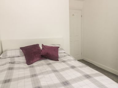 A bed with gray and white checkered bedding and two purple pillows in a room with a white door at 2 The Close in Robin Hoods Bay