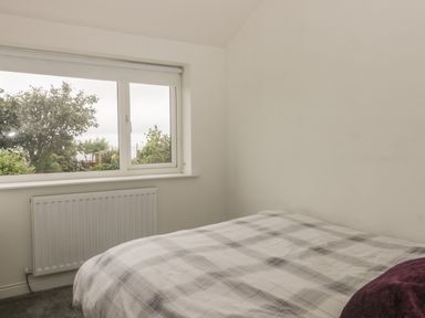 A bedroom with a bed covered in a plaid blanket near a window with a white radiator below the window at 2 The Close in Robin Hood'S Bay