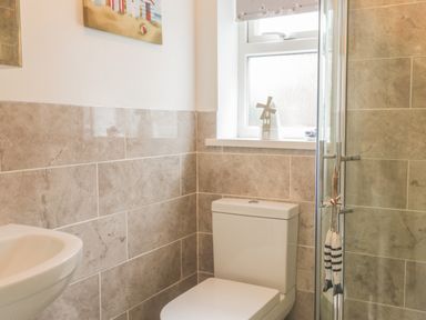 A bathroom with a toilet sink and shower with tiled walls and a window with a small decoration at 2 The Close in Robin Hood'S Bay