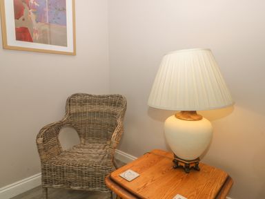A wicker chair next to a wooden side table with a lamp and framed artwork on the wall at 2 The Close in Robin Hood'S Bay