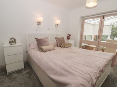 A bedroom with a double bed two bedside tables wall lamps and sliding glass doors leading to a conservatory at 2 The Close in Robin Hood'S Bay