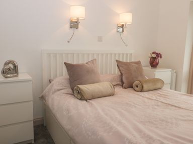 A bedroom with a bed with pink bedding and pillows two bedside tables with decorations and wall lights above at 2 The Close in Robin Hood'S Bay