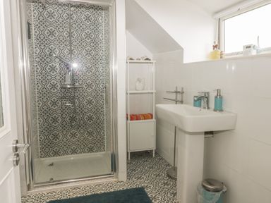 A bathroom with a shower cubicle with patterned tiles a white sink with soap dispenser and a small storage unit with towels and decor at 2 The Close in Robin Hood'S Bay