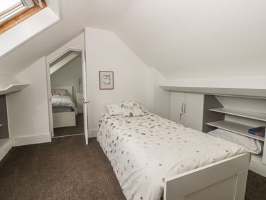 A bedroom with a single bed and polka dot bedding under a slanted ceiling with built-in shelves and a skylight at 2 The Close in Robin Hood'S Bay