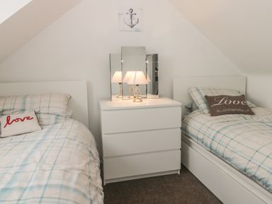 A bedroom with two single beds with plaid bedding and pillows that say love a white dresser with a lamp and a three panel mirror on top at 2 The Close in Robin Hood'S Bay