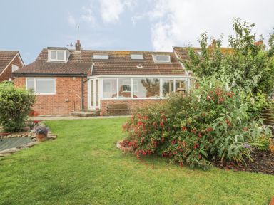 A backyard with green grass bushes and a brick house with a tiled roof at 2 The Close in Robin Hood'S Bay