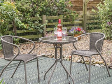 An outdoor patio with two wicker chairs and a small glass table with a bottle of wine and two wine glasses at 2 The Close in Robin Hood'S Bay
