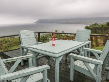 An outdoor deck with a wooden table and four chairs with a bottle of wine and two wine glasses overlooking the sea at 2 The Close in Robin Hood'S Bay