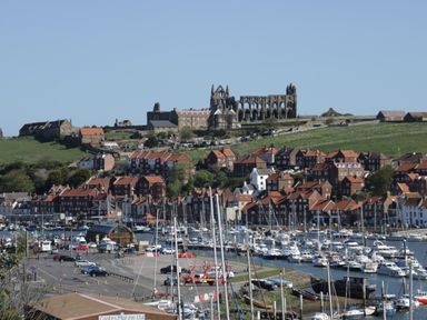 A marina with many boats docked near a town with red roof houses and a large historic abbey on a hill at 2 The Close in Robin Hood'S Bay