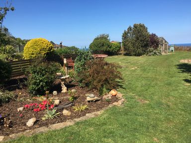 A garden with shrubs flowers a birdbath and lawn chairs near a greenhouse at 2 The Close in Robin Hood'S Bay