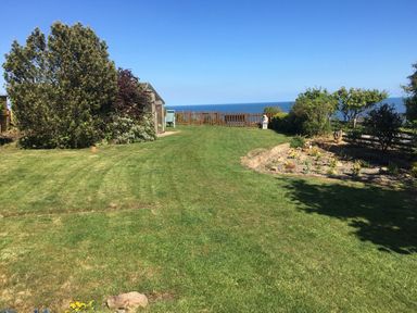 A grassy garden with a small greenhouse a wooden fence overlooking the sea and flower beds at 2 The Close in Robin Hood'S Bay