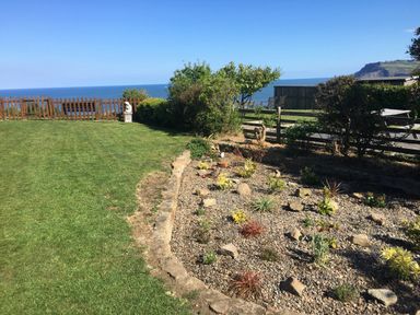 A garden with grass lawn and a rock garden with plants overlooking the sea with a wooden fence and bushes at 2 The Close in Robin Hood'S Bay