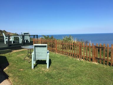 A grassy outdoor area with wooden chairs and tables near a wooden fence overlooking the sea at 2 The Close in Robin Hood'S Bay
