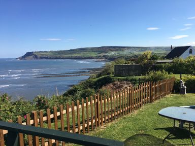 A fenced garden with a table and statue overlooking a bay and hillside at 2 The Close in Robin Hood'S Bay