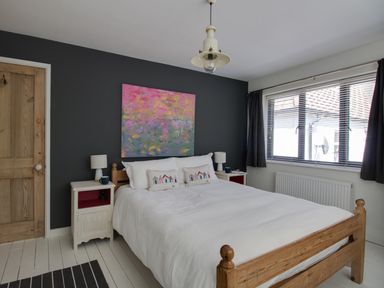 A bedroom with a wooden bed white bedding two bedside tables lamps and a colorful painting on a dark wall at Sailor's Watch in Weymouth