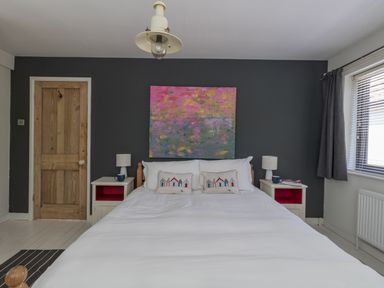 A bedroom with a bed two bedside tables lamps and a pink and green painting on a dark wall at Sailor's Watch in Weymouth