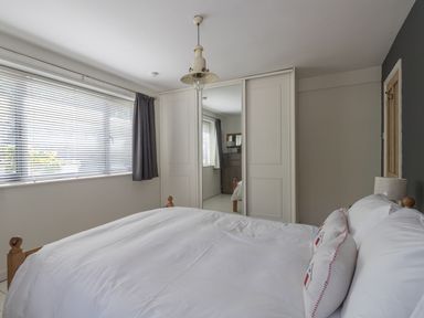 A bedroom with a bed, pillows, window with blinds and curtain, mirrored wardrobe doors, and a pendant light at Sailor's Watch in Weymouth