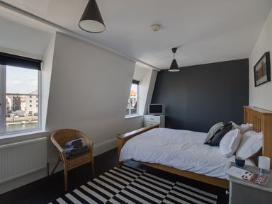 A bedroom with a wooden bed white linens striped rug a wicker chair with towels and a small TV at Sailor's Watch in Weymouth