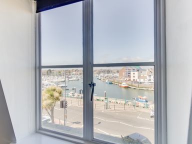 A window view of boats docked at a marina next to buildings and a street at Sailor's Watch in Weymouth