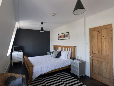 A bedroom with a wooden bed white bedding a striped rug a wooden door and two bedside tables at Sailor's Watch in Weymouth