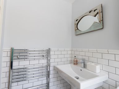 A bathroom with a wall-mounted white sink a chrome towel radiator and a fish-shaped mirror at Sailor's Watch in Weymouth