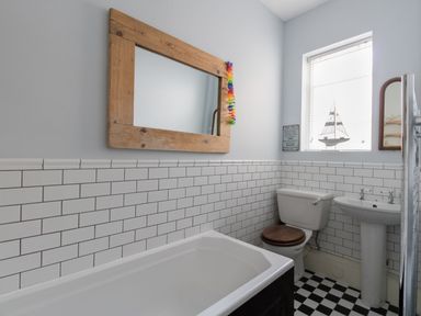 A bathroom with a bathtub toilet and sink with white tiles and a checkered black and white floor at Sailor's Watch in Weymouth