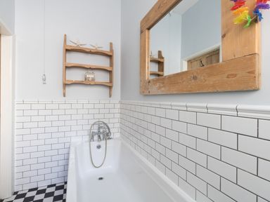 A bathroom with a white bathtub white subway tiles a wooden framed mirror and a wooden wall shelf at Sailor's Watch in Weymouth