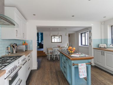A kitchen with a blue island, white cabinets, a dining table and chairs at Sailor's Watch in Weymouth