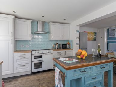 A kitchen with white cabinets a stove a blue tiled backsplash and a blue island with fruit in a bowl at Sailor's Watch in Weymouth