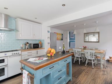 A kitchen with a blue island, stove, microwave, refrigerator, and dining table with chairs at Sailor's Watch in Weymouth