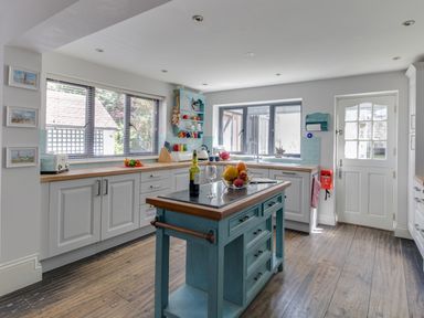 A kitchen with white cabinets a blue island a wooden countertop and windows at Sailor's Watch in Weymouth