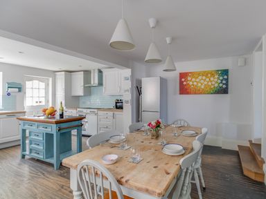 A kitchen and dining area with a wooden dining table set for six people a blue kitchen island and white cabinetry at Sailor's Watch in Weymouth