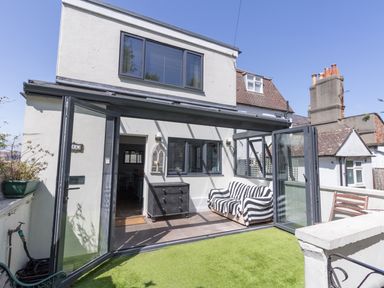 A small patio with open folding glass doors a striped sofa a black chest of drawers and artificial grass at Sailor's Watch in Weymouth
