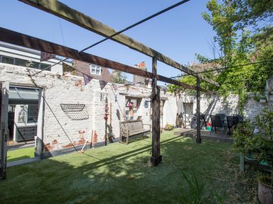 An outdoor courtyard with a wooden bench artificial grass a table with chairs and hanging bunting at Sailor's Watch in Weymouth