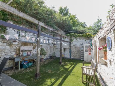 An outdoor enclosed garden area with stone walls bench table and string lights at Sailor's Watch in Weymouth