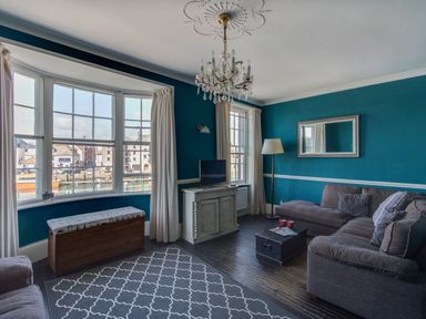 A living room with a gray sectional sofa a wooden chest and a patterned rug at Sailor's Watch in Weymouth