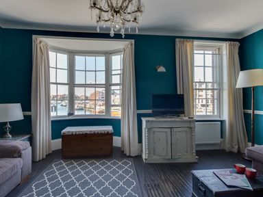 A living room with a television on a cabinet a wooden chest under a bay window and a patterned rug on the floor at Sailor's Watch in Weymouth