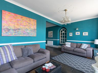 A living room with two sofas a coffee table with cups books a rug and paintings on the walls at Sailor's Watch in Weymouth