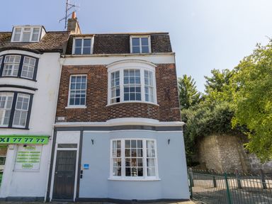 A three-story building with brick and painted exterior next to a taxi office and a stone wall with trees at Sailor's Watch in Weymouth