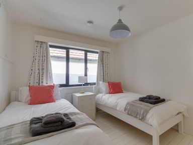 A bedroom with two single beds with white bedding and coral pillows and folded towels on each bed at Sailor's Watch in Weymouth